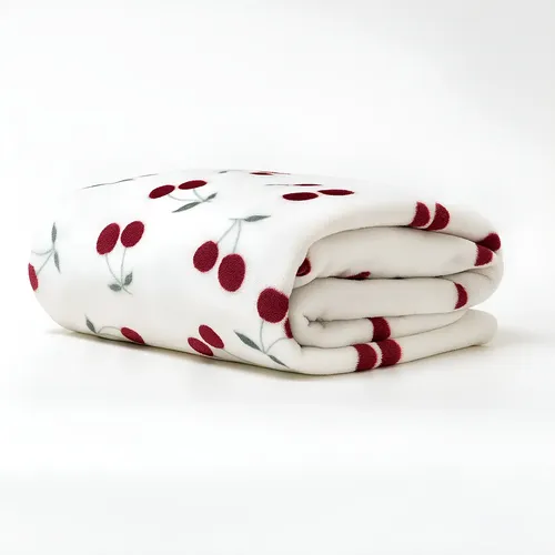 Manta Flannel Soft branca dobrada com estampa de cerejas vermelhas e galhos verdes, em close-up, sobre fundo branco.