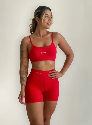 Mulher vestindo conjunto fitness vermelho composto por top de alças finas e shorts meia coxa de cintura alta contra fundo neutro