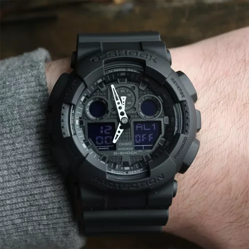 Reloj de pulsera Casio G-Shock GA100 de cuerpo color negro,  analógico-digital, para hombre, fondo camuflado gris, con correa de resina  color negro, agujas color azul y blanco, dial gris, subesferas color gris