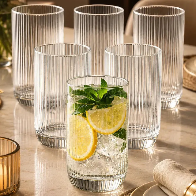 Conjunto de seis copos de vidro canelado de 400ml dispostos sobre uma mesa, com um dos copos contendo gelo, rodelas de limão e hortelã.