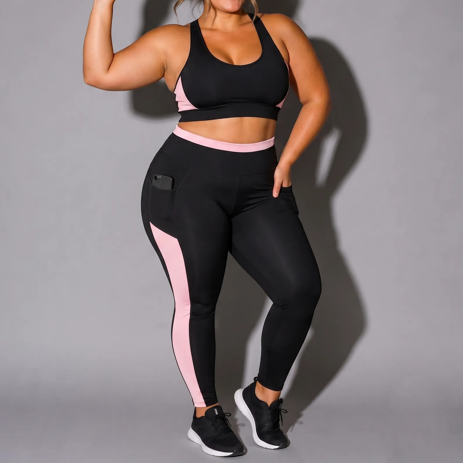 Modelo plus size vestindo conjunto fitness preto com detalhes em rosa, composto por top e calça com bolso lateral para celular