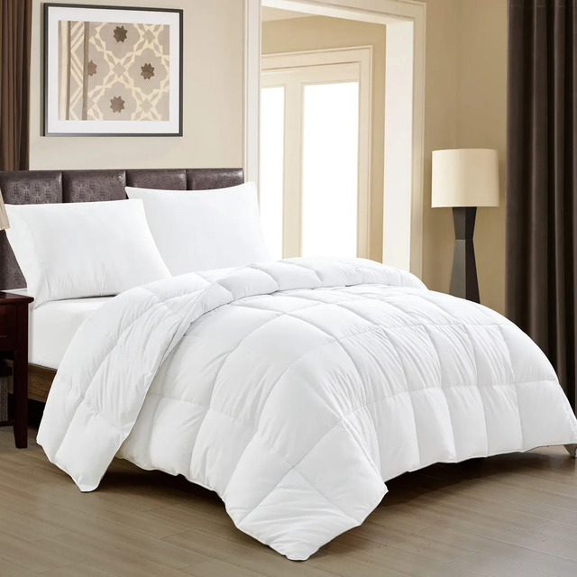 Edredom de casal branco dupla face com costura em gomos, sobre uma cama organizada em um quarto aconchegante com luminária e quadro na parede.