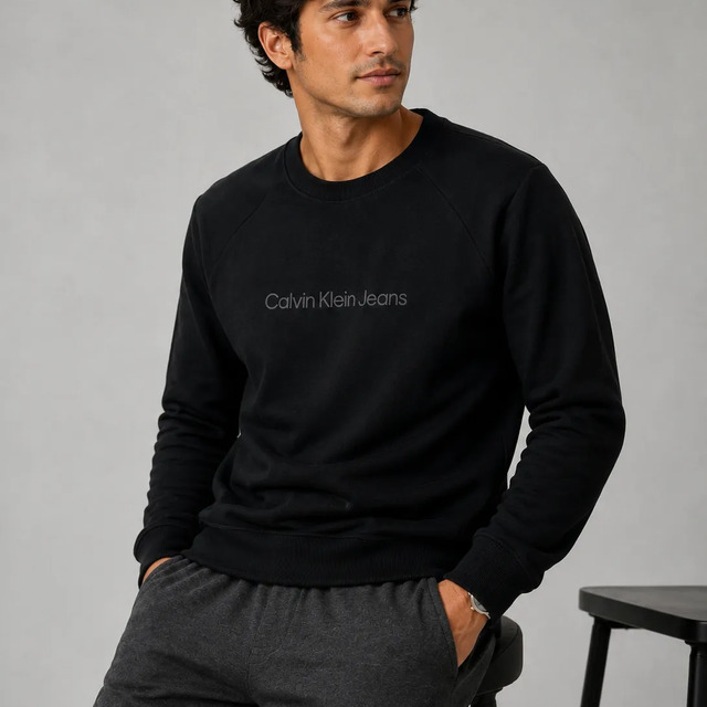 Homem vestindo moletom preto da Calvin Klein com gola careca e logo frontal discreto, sentado em um banco