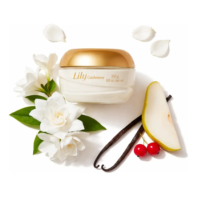 Pote de creme acetinado O Boticário Lily Cashmere de 250g com tampa dourada, cercado por flores brancas, uma fatia de pera e favas de baunilha sobre fundo branco.