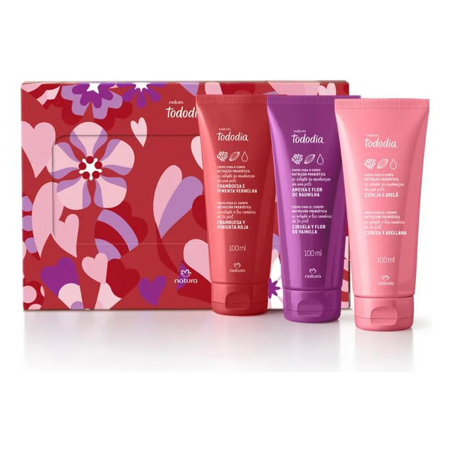 Conjunto de presente Natura Tododia com três bisnagas de hidratantes corporais de 100ml cada, nas fragrâncias Framboesa e Pimenta Vermelha, Ameixa e Flor de Baunilha e Cereja e Avelã, dispostas à frente de uma caixa decorada com estampa floral e corações.