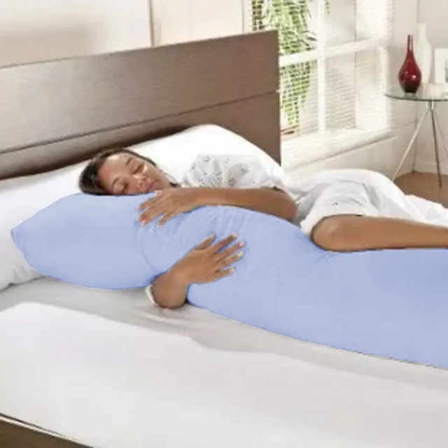 Mulher deitada na cama abraçada a um travesseiro de corpo longo na cor azul claro