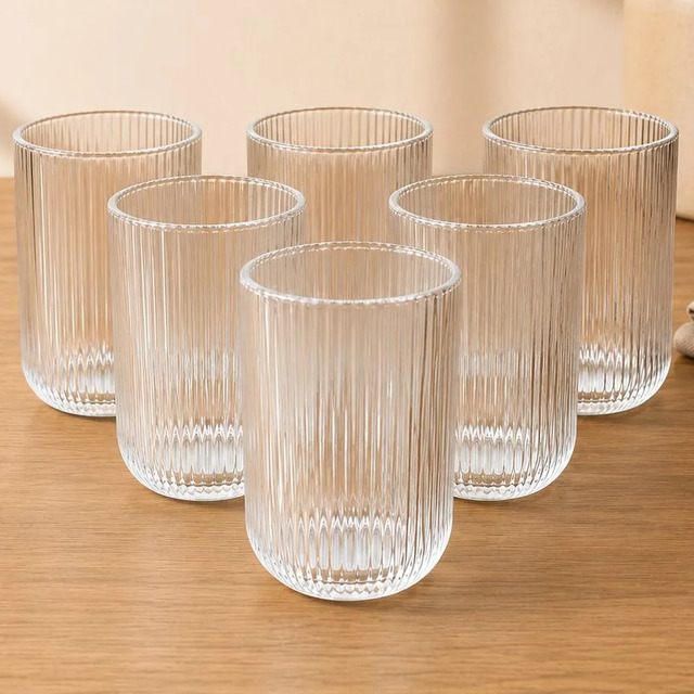 Conjunto de seis copos de vidro com design canelado e base arredondada dispostos sobre uma superfície de madeira clara.