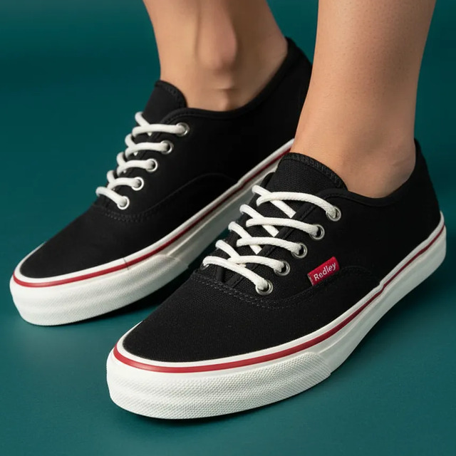 Par de tênis Redley Ir10 Originals na cor preta com solado branco e detalhe de linha vermelha, exibidos em um fundo verde escuro.