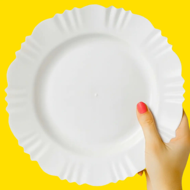 Mão segurando um prato de plástico branco com bordas em formato de pétala sobre fundo amarelo