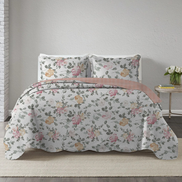 Colcha king com estampa floral delicada e acabamento matelasse, em cores pastéis, sobre uma cama com dois travesseiros combinados.
