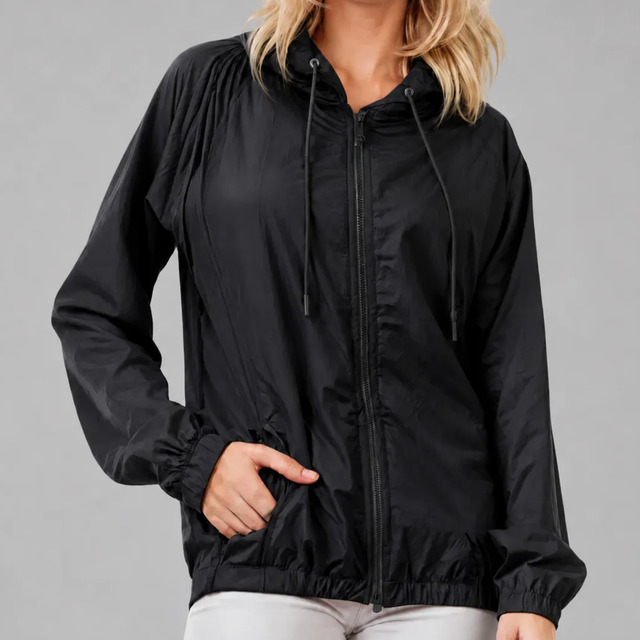 Jaqueta feminina preta com capuz e zíper, exibindo design leve, bolsos laterais e punhos elásticos em fundo cinza neutro.