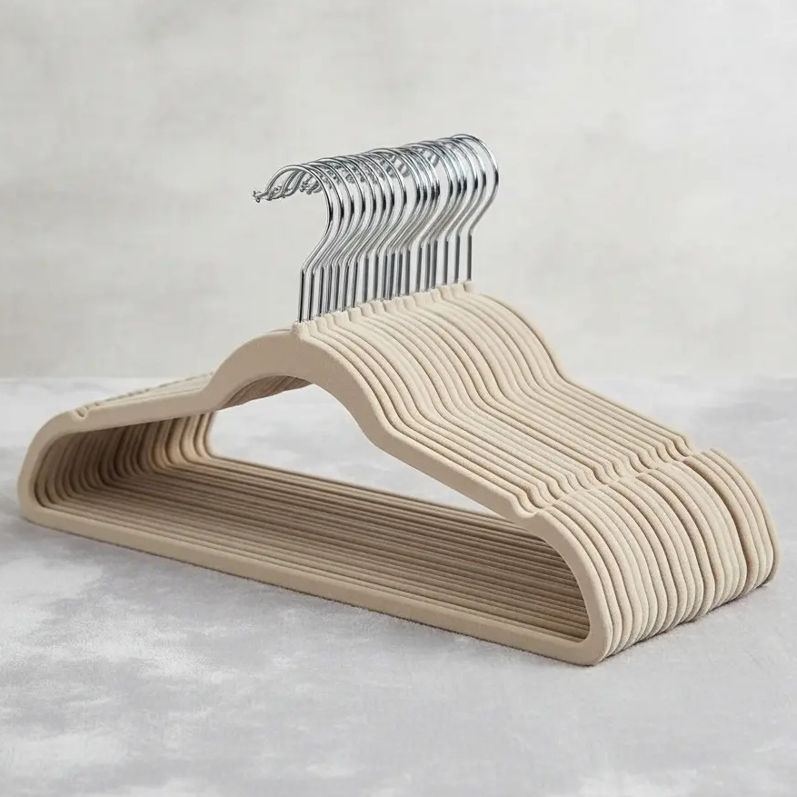 Conjunto de 50 cabides slim com revestimento de veludo bege e ganchos cromados dispostos em uma superfície clara