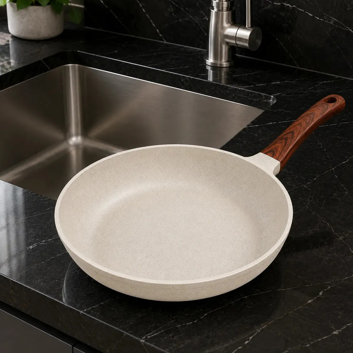 Frigideira de cerâmica antiaderente na cor creme com cabo efeito madeira, posicionada sobre uma bancada de granito preto ao lado de uma pia de inox.