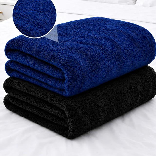 Duas mantas de casal dobradas sobre uma cama, uma na cor azul royal e outra na cor preta, com um detalhe circular em destaque mostrando a textura aveludada do tecido.