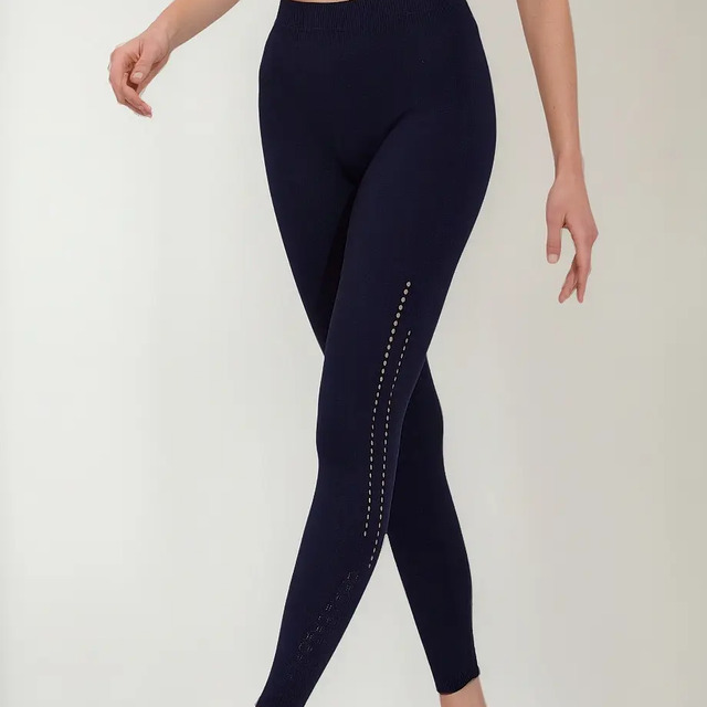 Modelo vestindo calça legging esportiva azul marinho da marca Trifil com detalhe de textura colmeia lateral e tênis branco