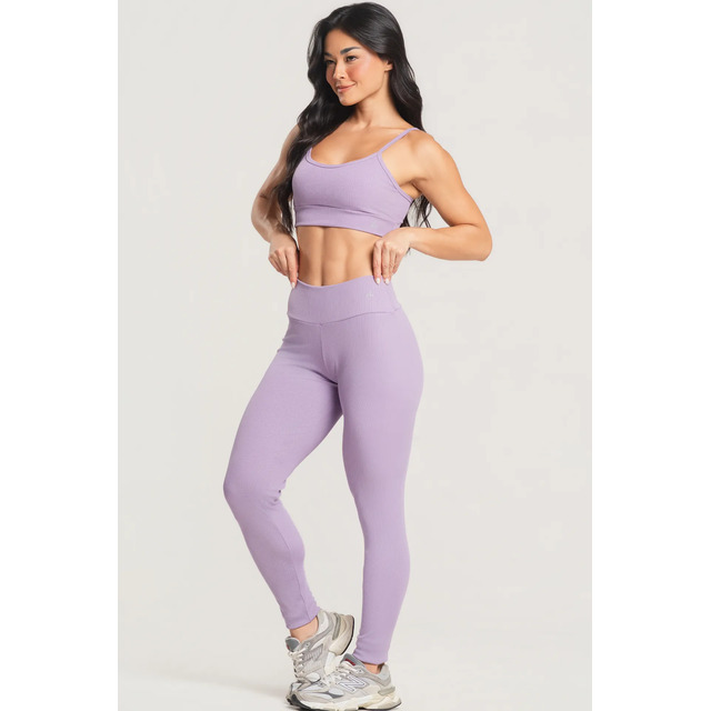 Modelo vestindo conjunto fitness lilás composto por top e calça legging canelada de cintura alta em fundo neutro
