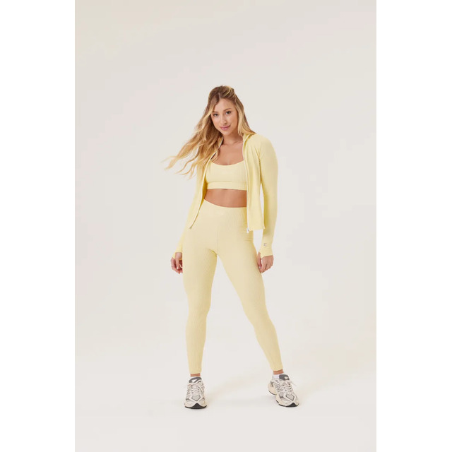 Modelo vestindo conjunto fitness amarelo com jaqueta de zíper e legging em fundo neutro