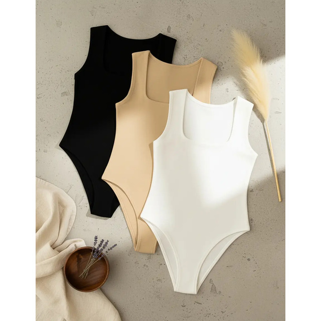 Kit de três bodies regata plus size nas cores preta, bege e branca, dispostos sobre uma superfície neutra ao lado de uma decoração minimalista