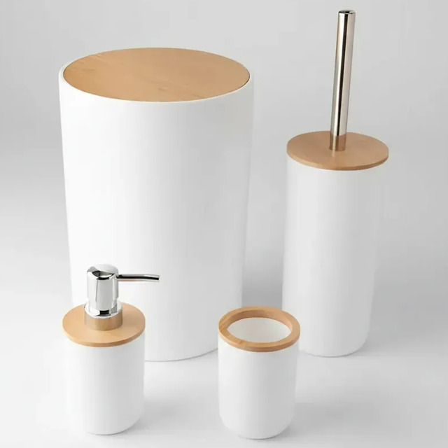 Kit de banheiro com 4 peças na cor branca com tampas de bambu, incluindo lixeira, porta-escovas, porta-sabonete líquido e copo organizador sobre fundo cinza claro.