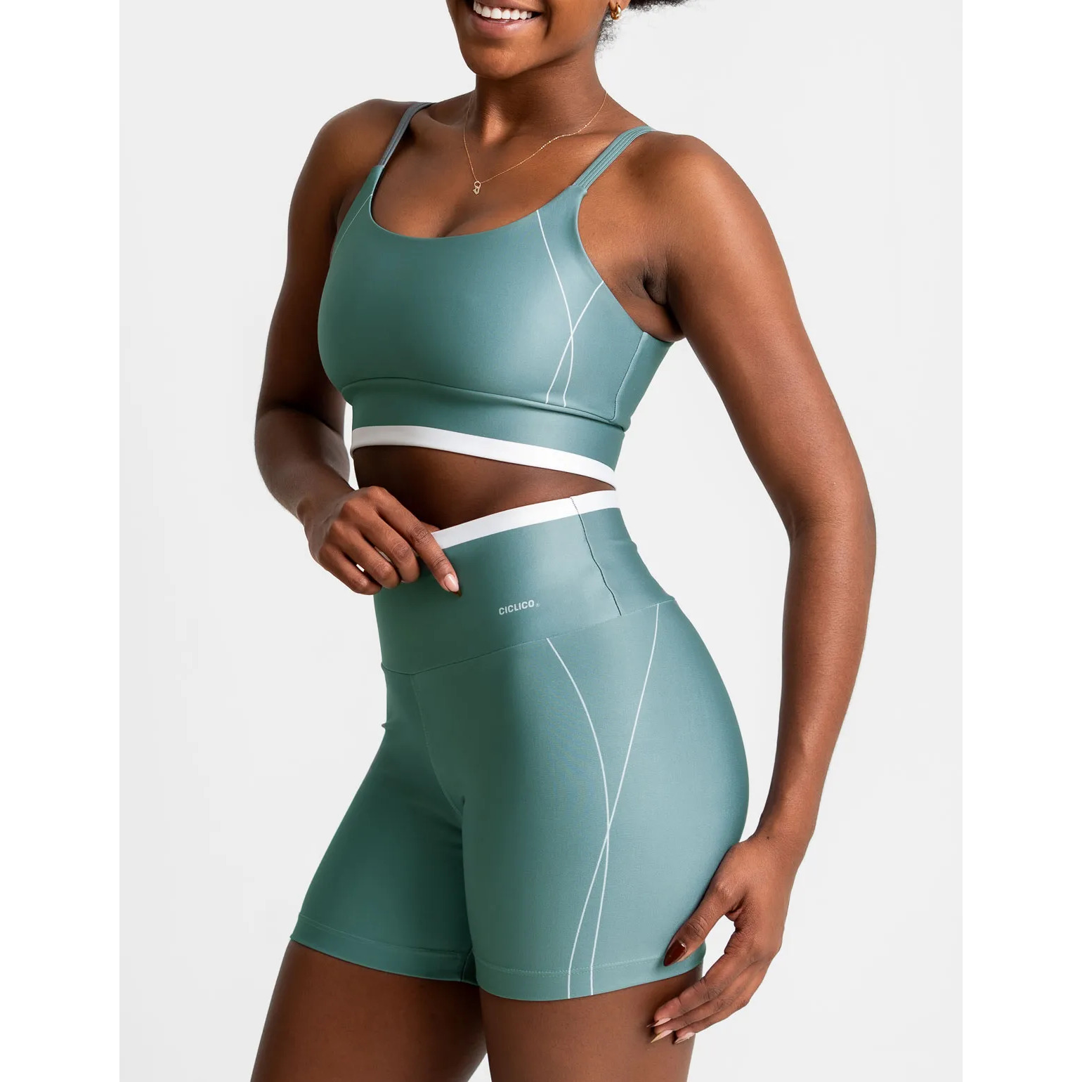 Modelo vestindo conjunto fitness Cíclico na cor verde, composto por top de alcinha e shorts com cós alto e detalhes em branco.