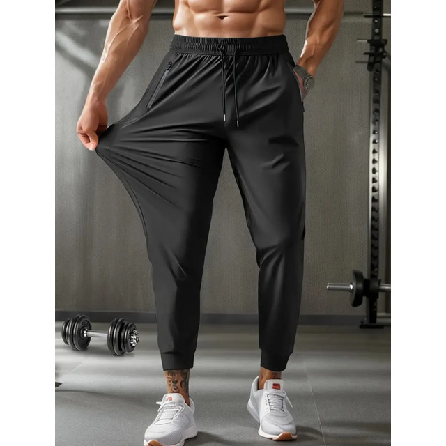 Homem atlético vestindo calça jogger preta esportiva com tecido elástico em ambiente de academia
