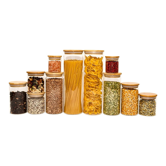 Conjunto de 11 potes de vidro de diversos tamanhos com tampas de bambu contendo diferentes mantimentos como massas, grãos e especiarias dispostos em ordem crescente