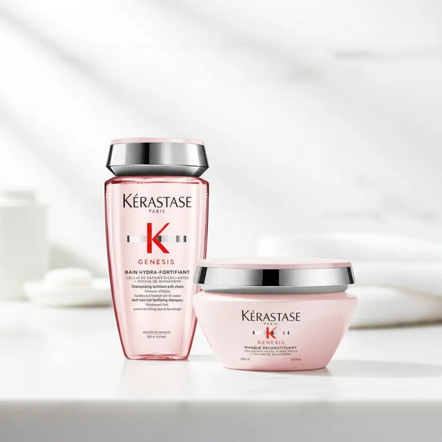 Kit Kérastase Genesis contendo um frasco de shampoo rosa translúcido e um pote de máscara capilar rosa em uma superfície branca com fundo desfocado