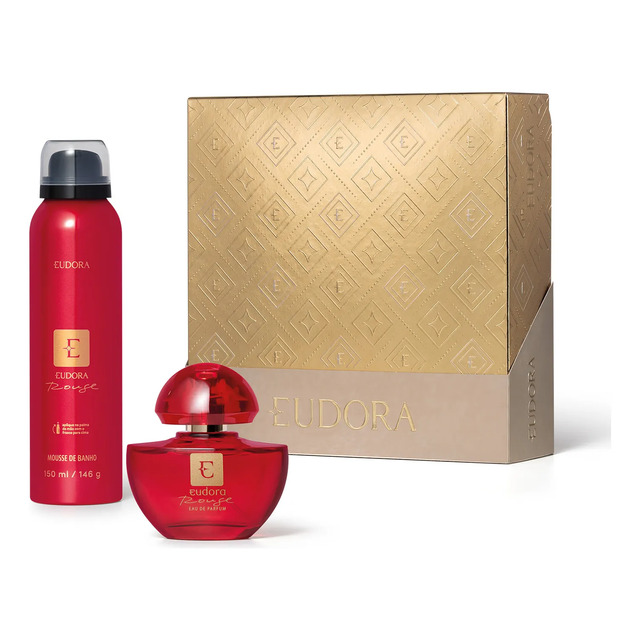 Kit Eudora Rouge contendo um frasco de perfume Eau de Parfum e um frasco de Mousse de Banho posicionados à frente de uma caixa de presente dourada com textura geométrica.