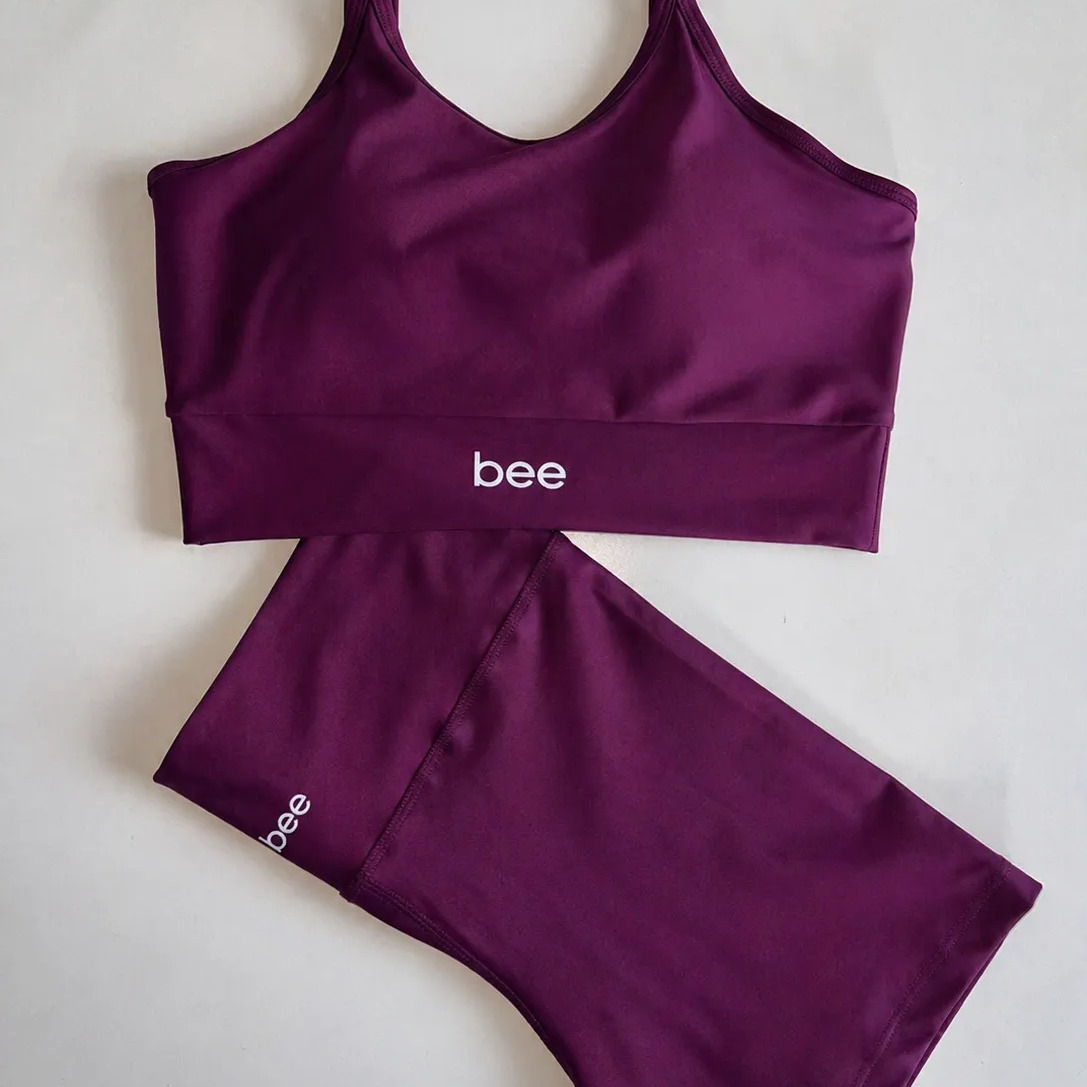 Conjunto fitness feminino da marca Bee na cor roxa, composto por um top cropped e um short, ambos com o logotipo da marca estampado.
