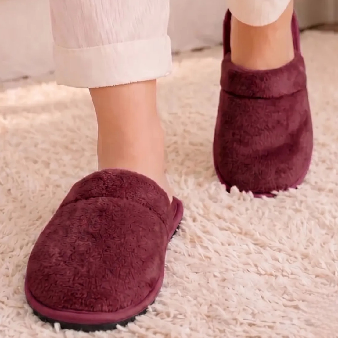 Pés calçando pantufa chinelo de quarto unissex na cor bordô com textura macia sobre tapete claro