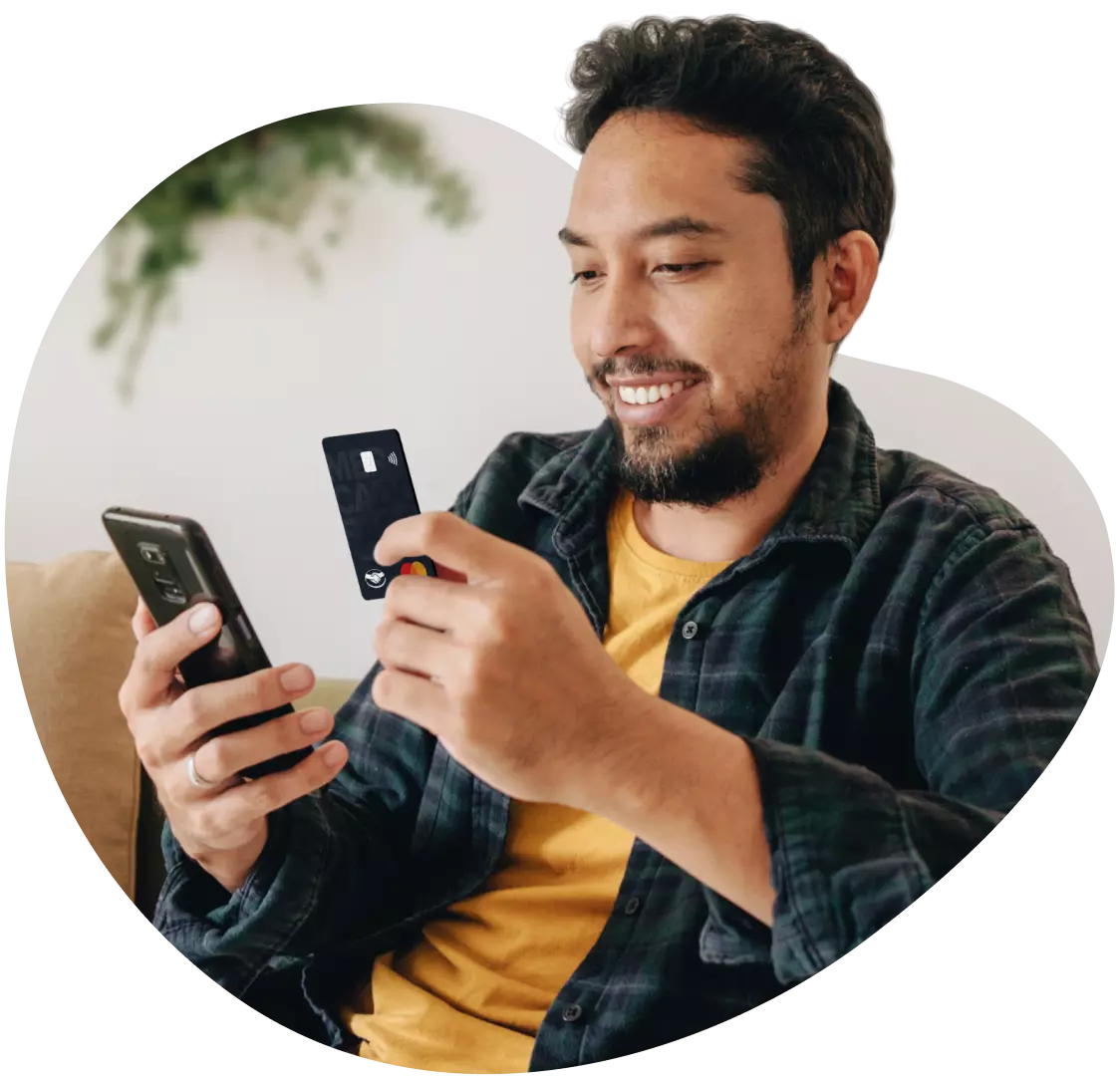 Homem feliz com um celular em uma mão e um cartão de crédito em outra.