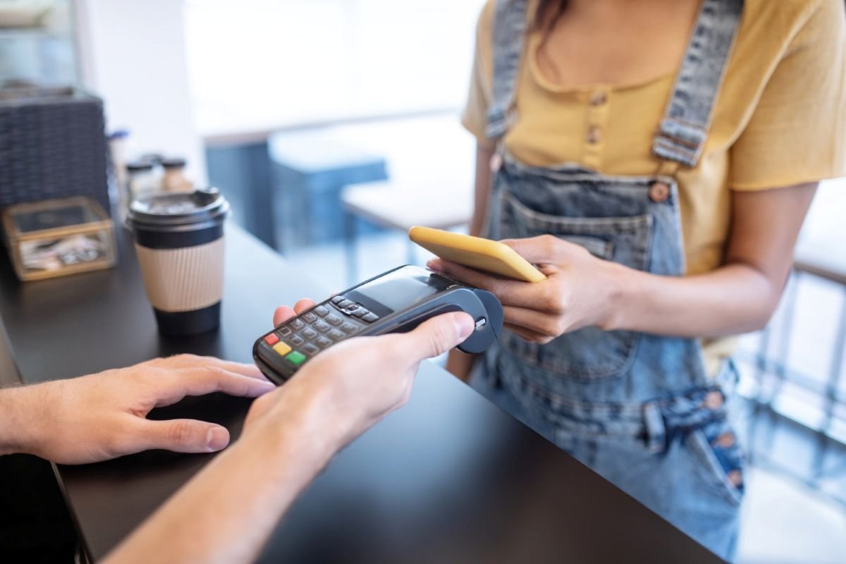 Cliente pagando por aproximação com o celular em maquininha de cartão.