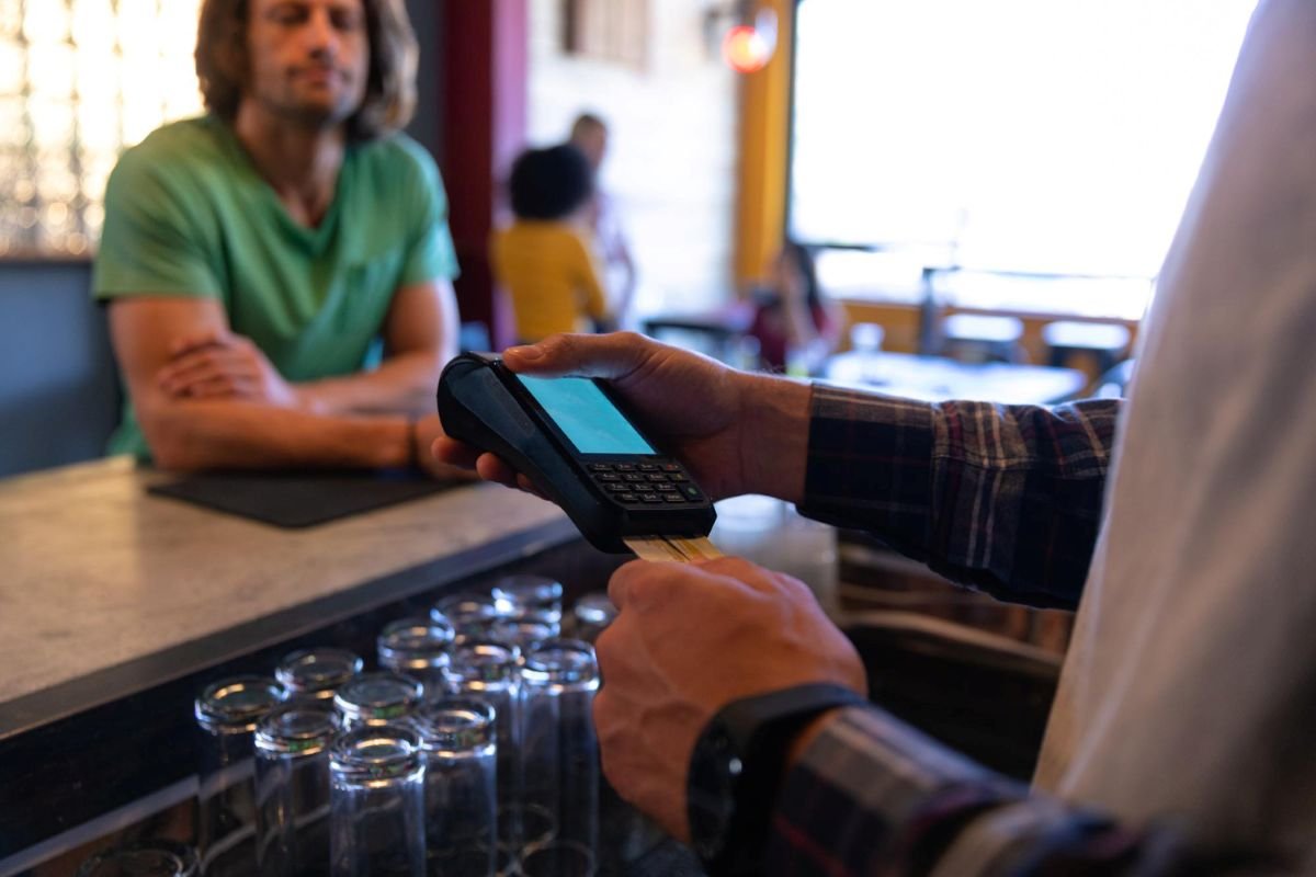 Comerciante usando maquininha de cartão com tela touchscreen em balcão de bar