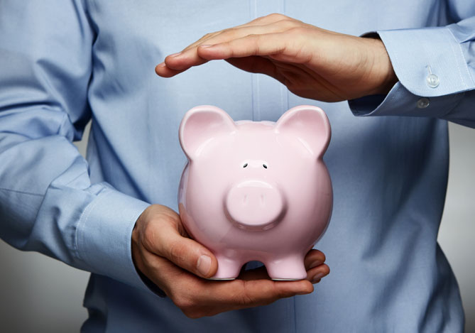 Mãos de um homem vestindo camisa social azul segurando um cofrinho no formato de um porquinho rosa para a pessoa buscar mais proteção financeira com o Seguro Limite Protegido do Mercado Pago.