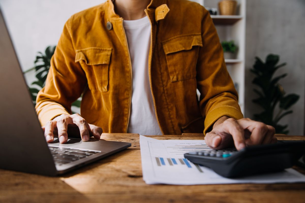 Homem em mesa mexe em laptop e calculadora