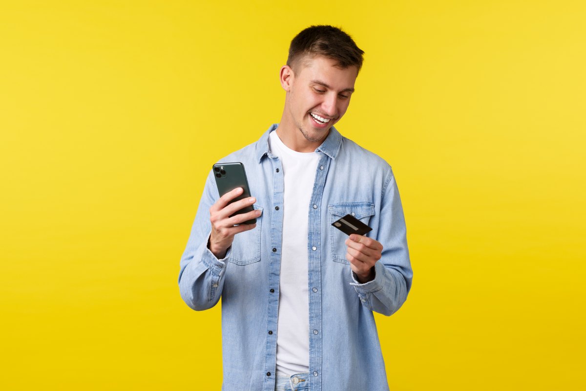 Hombre sosteniendo un teléfono y una tarjeta sobre fondo amarillo