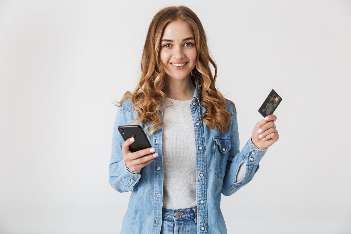 Persona sonriendo con tarjeta de crédito en una mano y celular en la otra