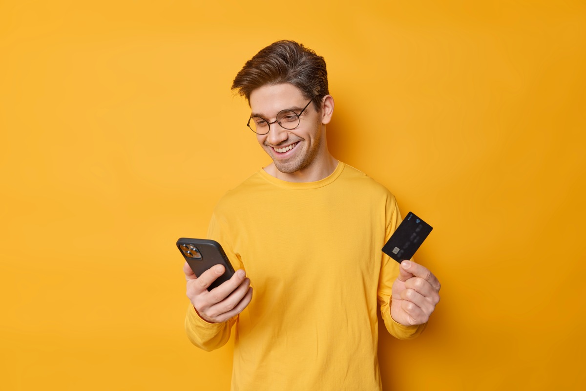 Pessoa segurando cartão e celular fazendo pagamento online