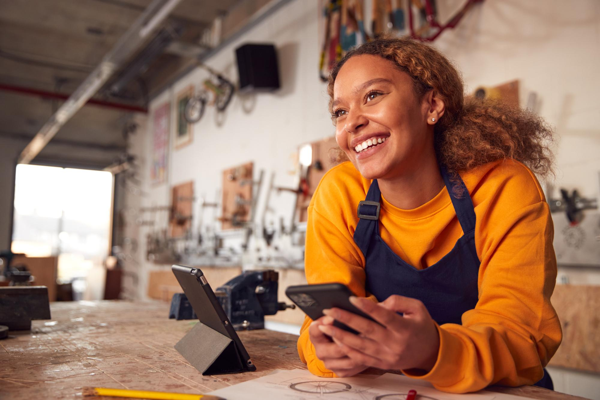 Empreendedora sorrindo em oficina com celular e tablet