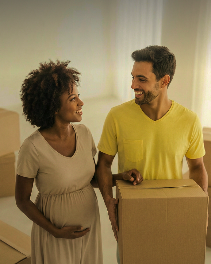 Casal sorridente carregando caixas de mudança em uma sala iluminada