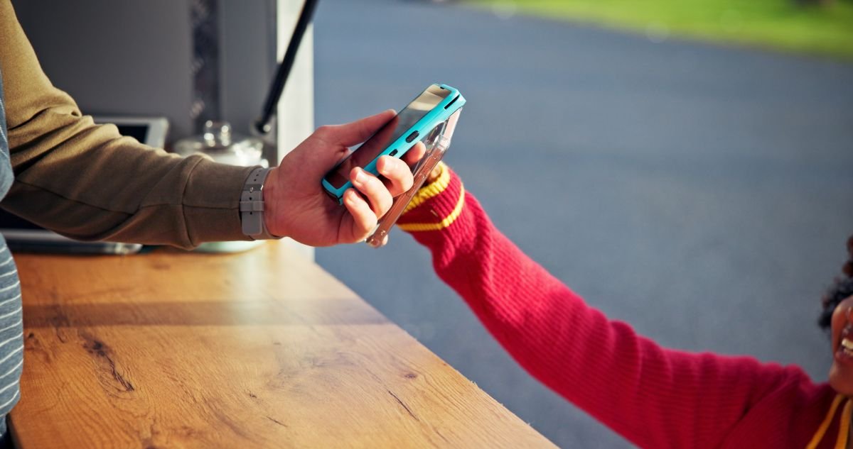 Empreendedor segurando a Point Mini NFC 2 enquanto cliente aproxima celular para pagamento