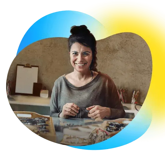 Una mujer sonriendo, sentada tras una mesa con pulseras de abalorios.