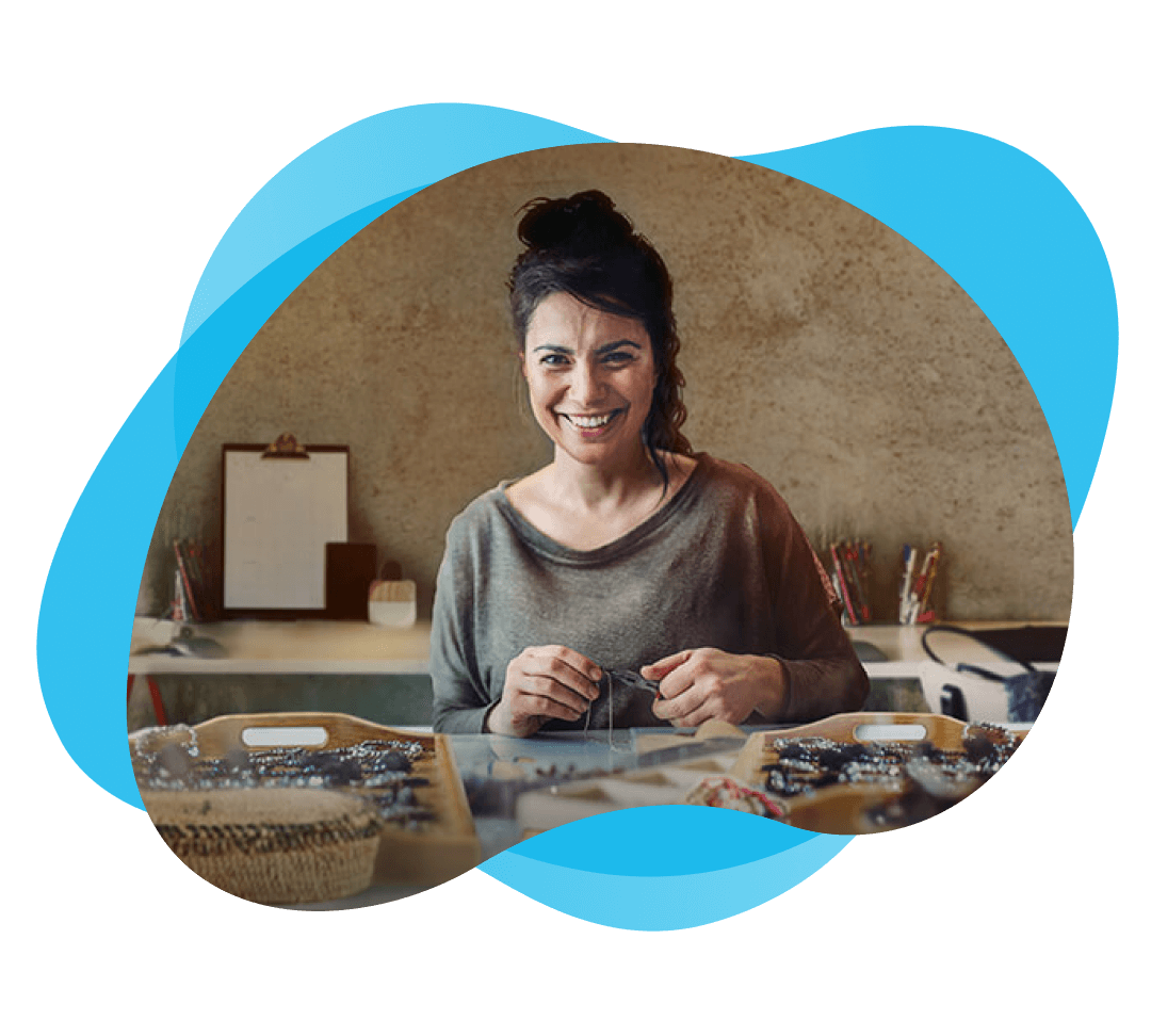 Una mujer sonriendo, sentada tras una mesa con pulseras de abalorios