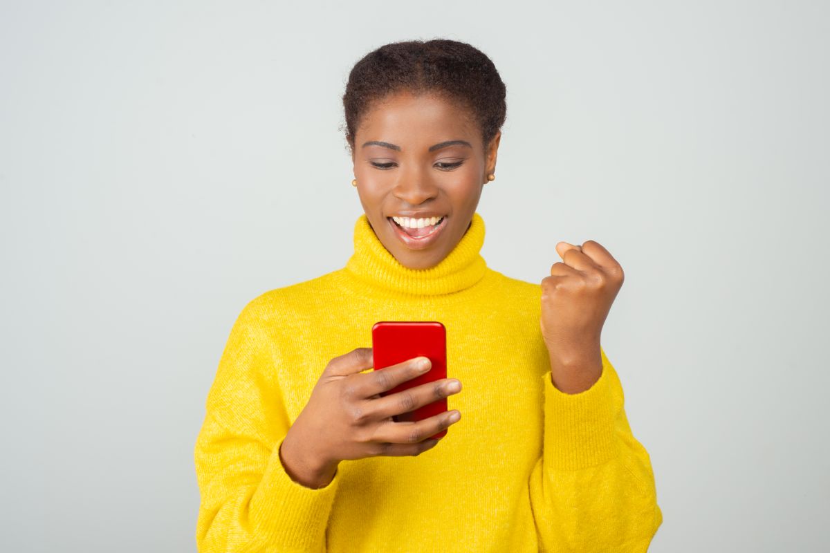 Mulher sorrindo enquanto segura celular e comemora pagamento online.