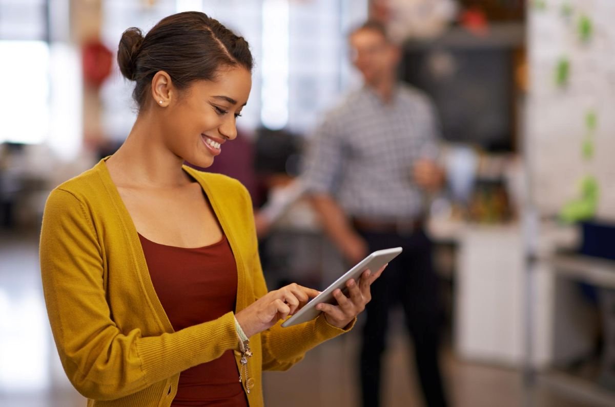 Lojista sorrindo enquanto envia mensagem pelo tablet para cliente após uma venda.