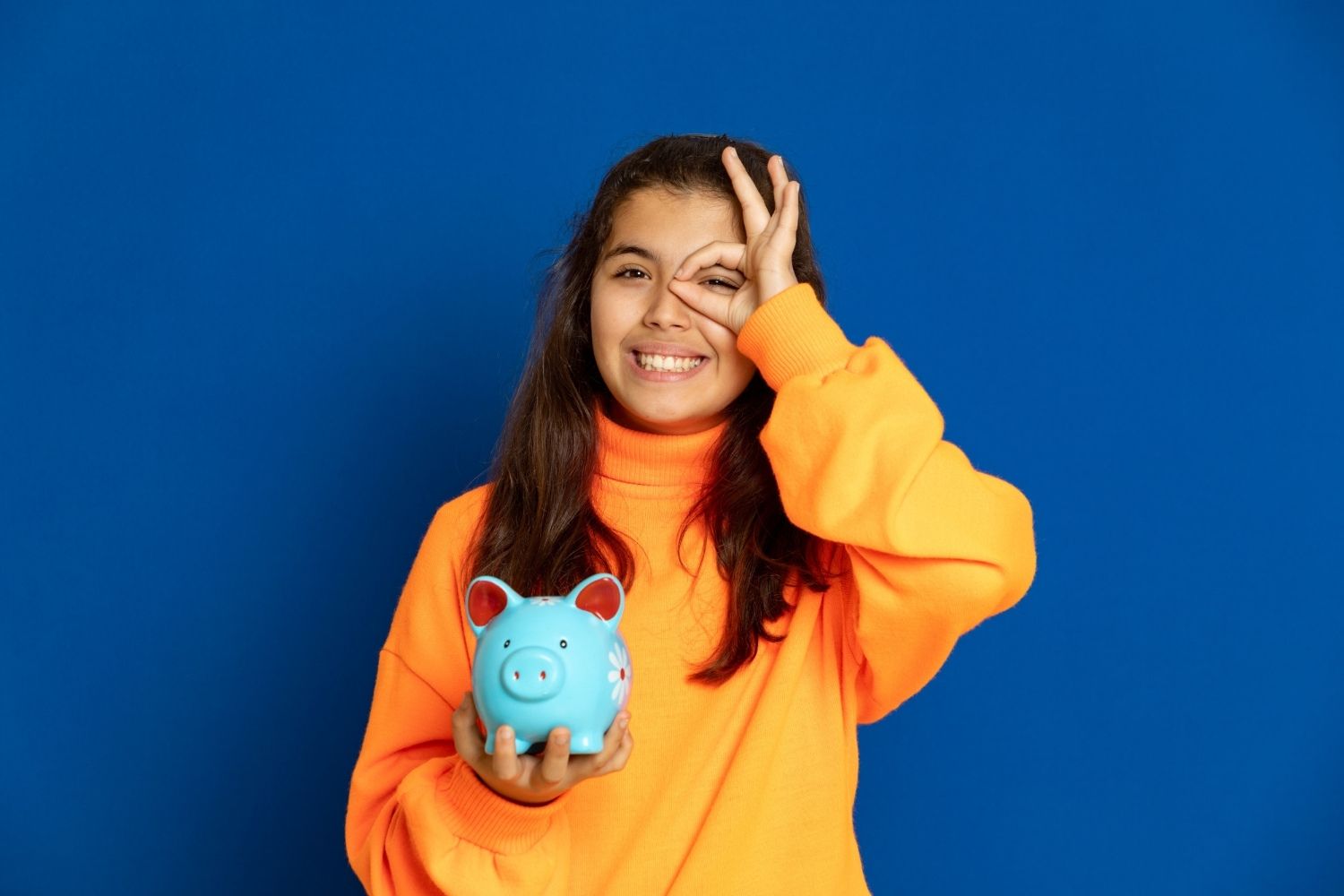 Jovem menina segurando um cofrinho e juntando dinheiro