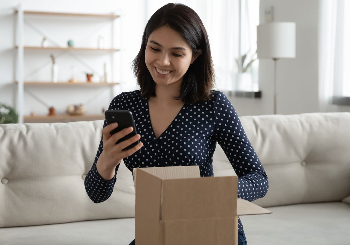 Mulher sorrindo com encomenda aberta e mexendo no smartphone