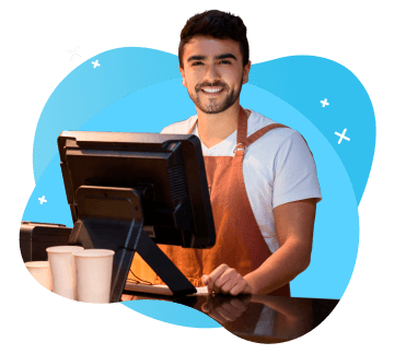 Un vendedor usando un delantal, detrás de la computadora de su tienda, sonriendo.
