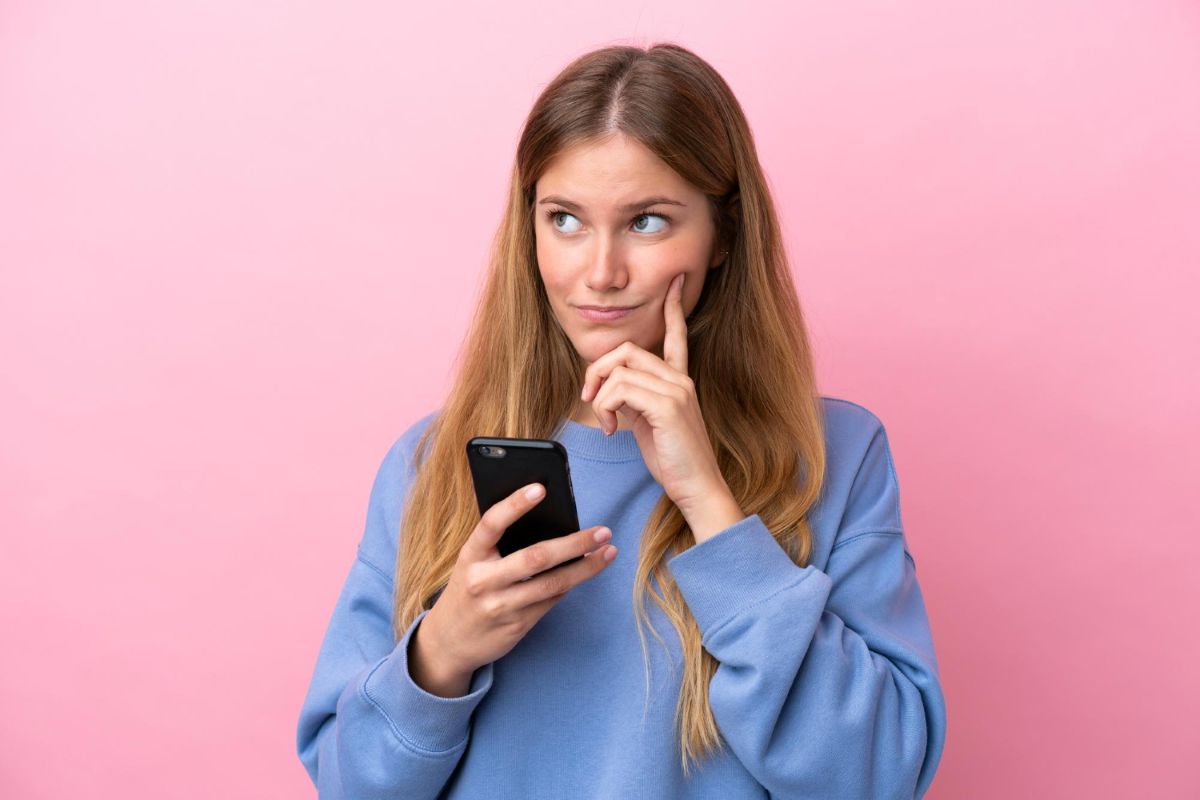 Mulher com celular em dúvida se paga o mínimo da fatura do cartão de crédito