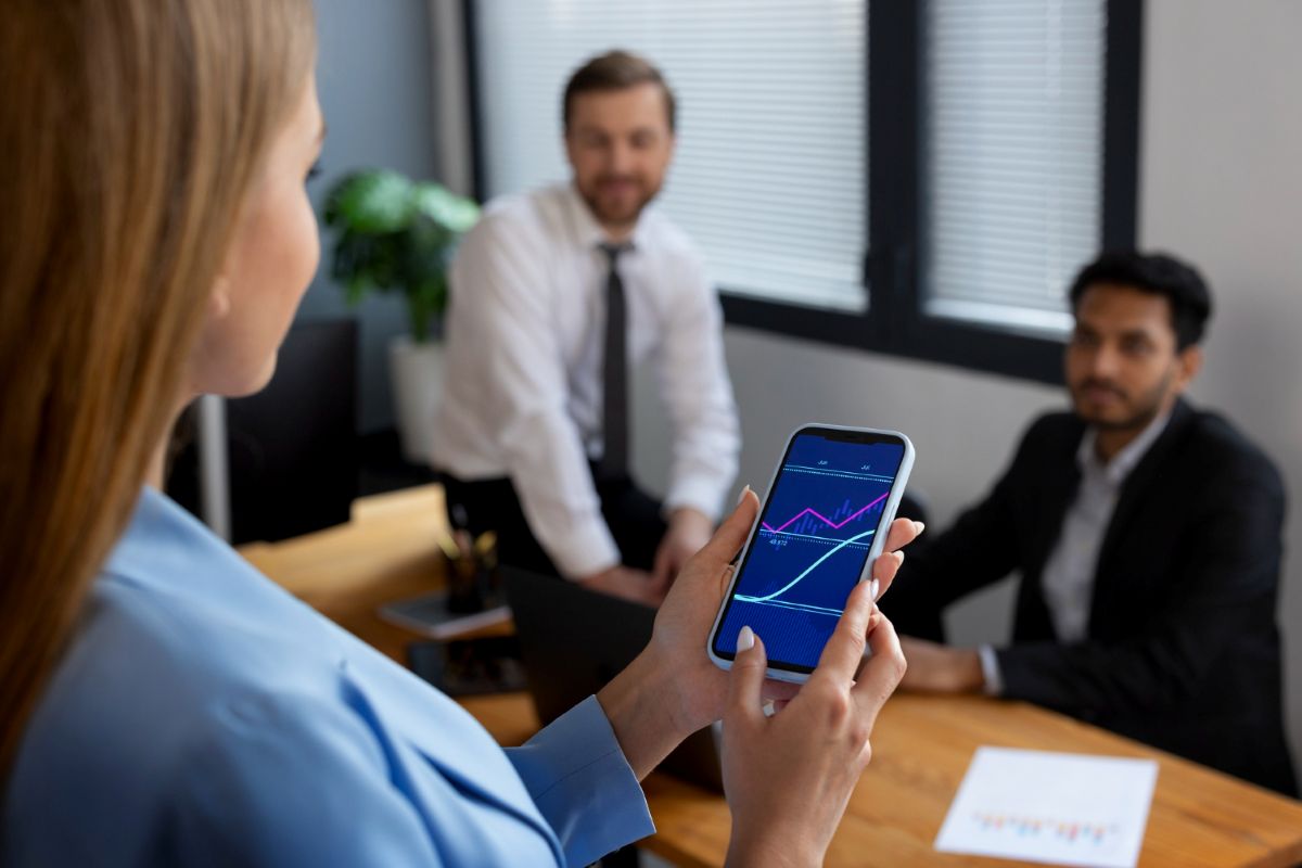 Mulher observa gráficos no celular em sala de reunião